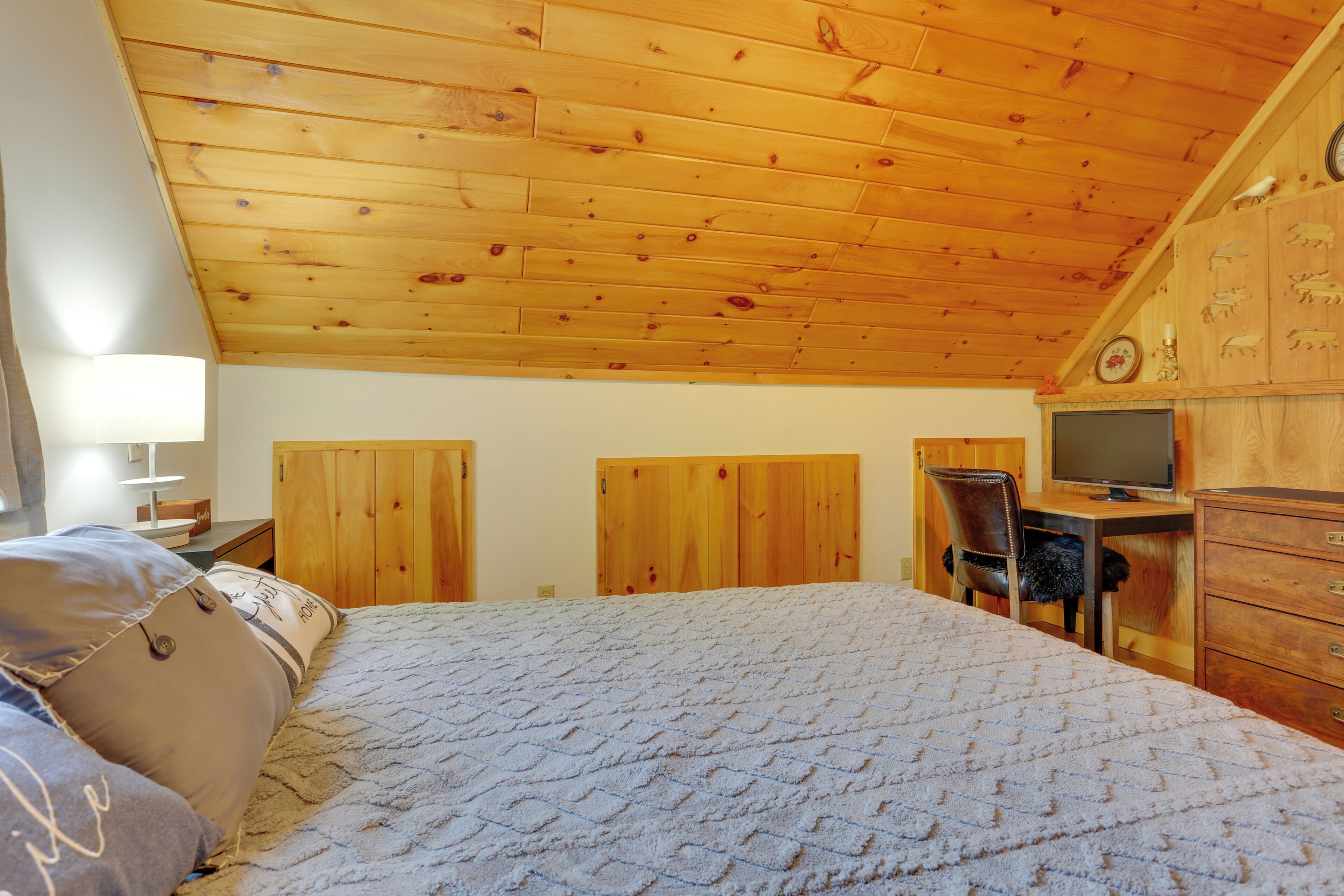 A bedroom with a wooden ceiling, a bed with a quilt, a desk with a computer, and a dresser.