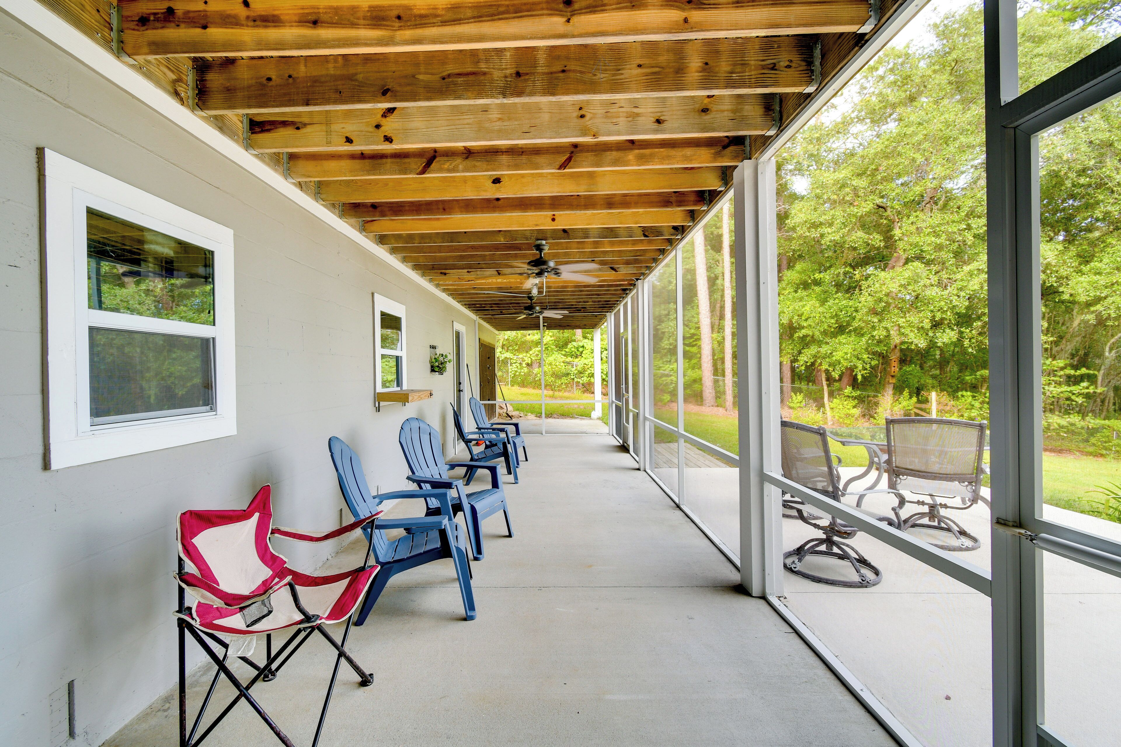 A covered outdoor seating area with chairs and tables, large windows, and a wooden ceiling.