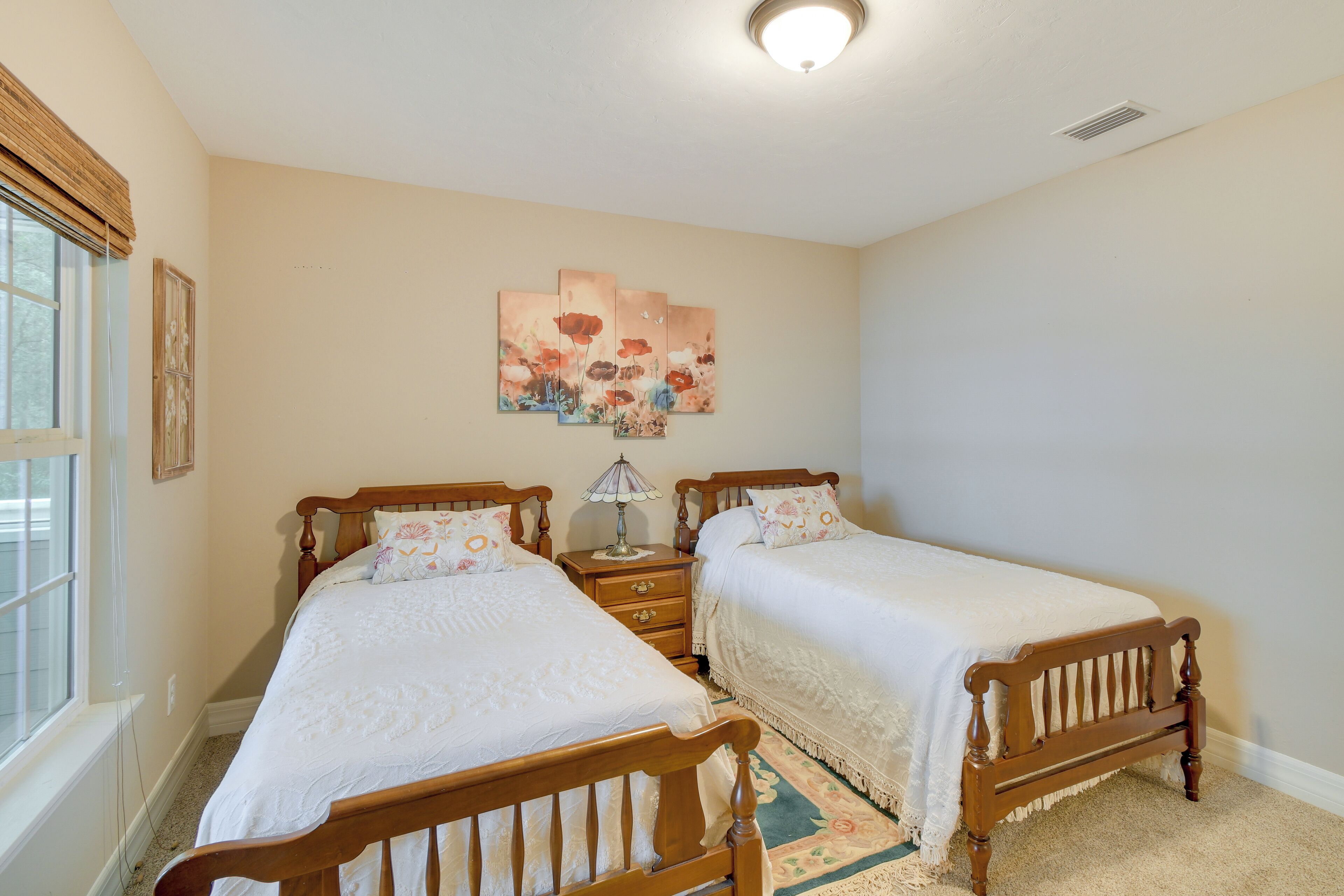 A bedroom with two wooden beds, a nightstand, a lamp, and a floral artwork on the wall.