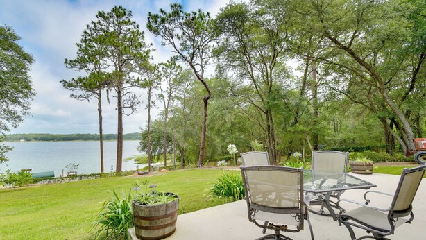 A patio with a glass table and chairs overlooking a lake, surrounded by trees. - Hawthorne Vacation Rental w/ Access to Cue Lake (Hawthorne)