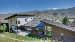 A modern two-story house with large windows, a flat roof, and a view of mountains in the background. - Avon Vacation Rental w/ Hot Tub & Mountain Views! (Avon)