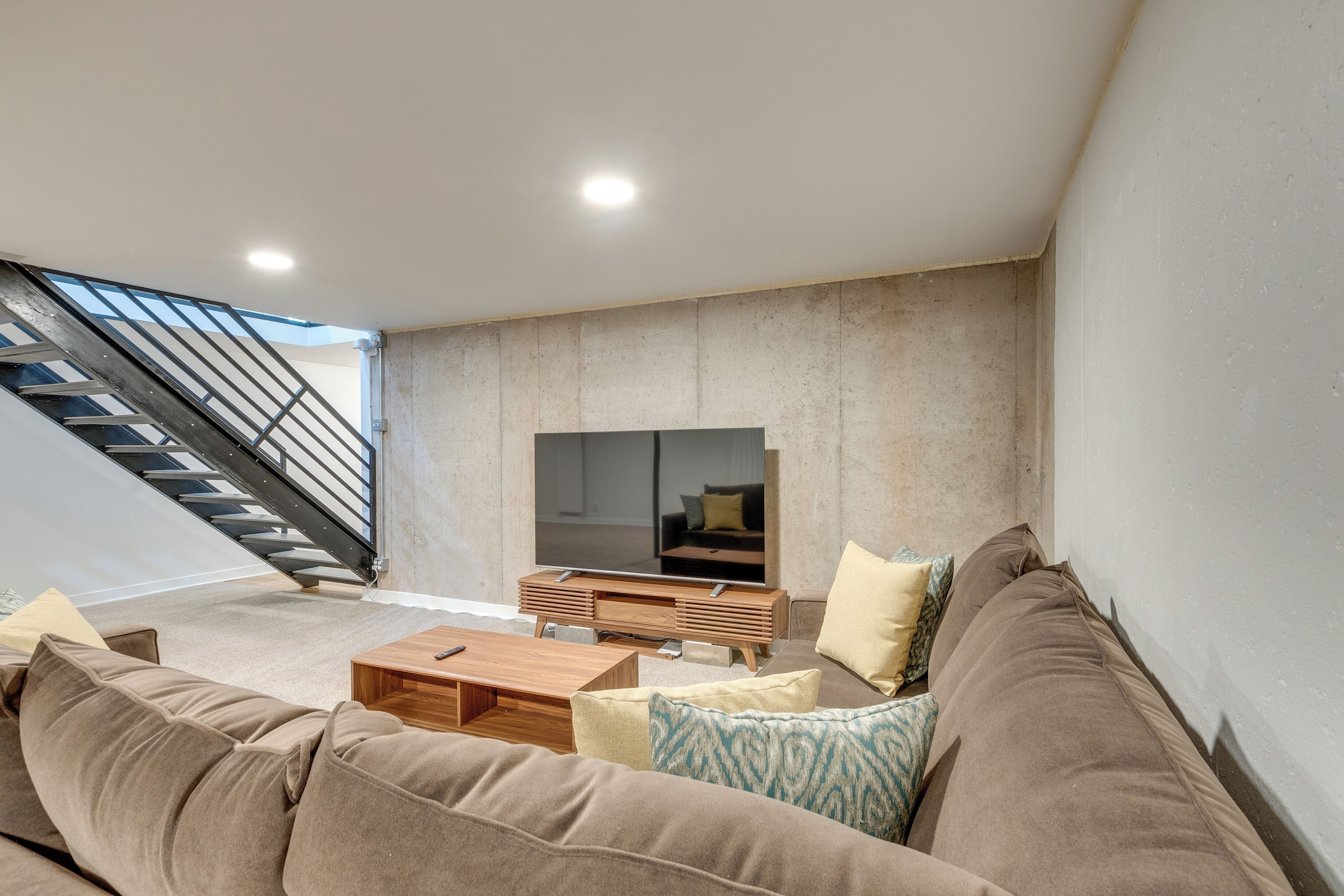 A modern living room with a staircase, a flat-screen TV, a wooden coffee table, and a large sofa.