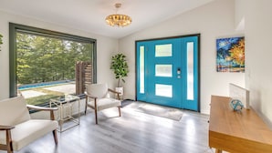 A modern living room with a large window, a blue door, and a wooden table. - Riverfront Appleton Home With Pool & Boat Dock! (Appleton)