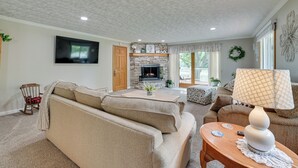 A living room with a stone fireplace, a television mounted on the wall, and a cozy seating area with a sofa and armchairs. - Northern Michigan Vacation Rental Near Trails! (Atlanta)