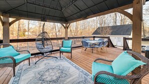 En overdækket terrasse med fletningsmøbler, et mønstret tæppe og udsigt over det omkringliggende landskab.