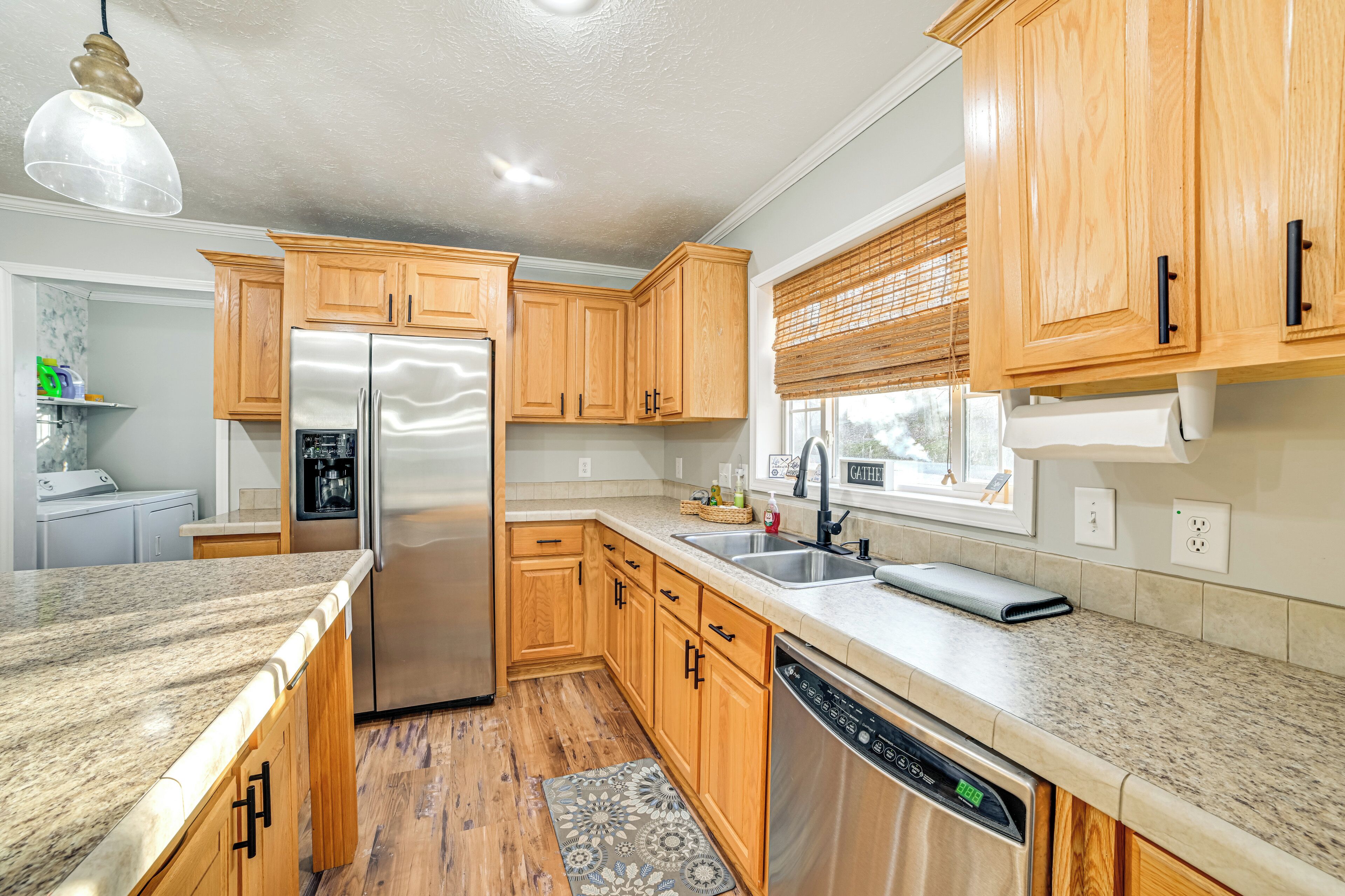 A modern kitchen with wooden cabinets, stainless steel appliances, granite countertops, and a window with blinds.