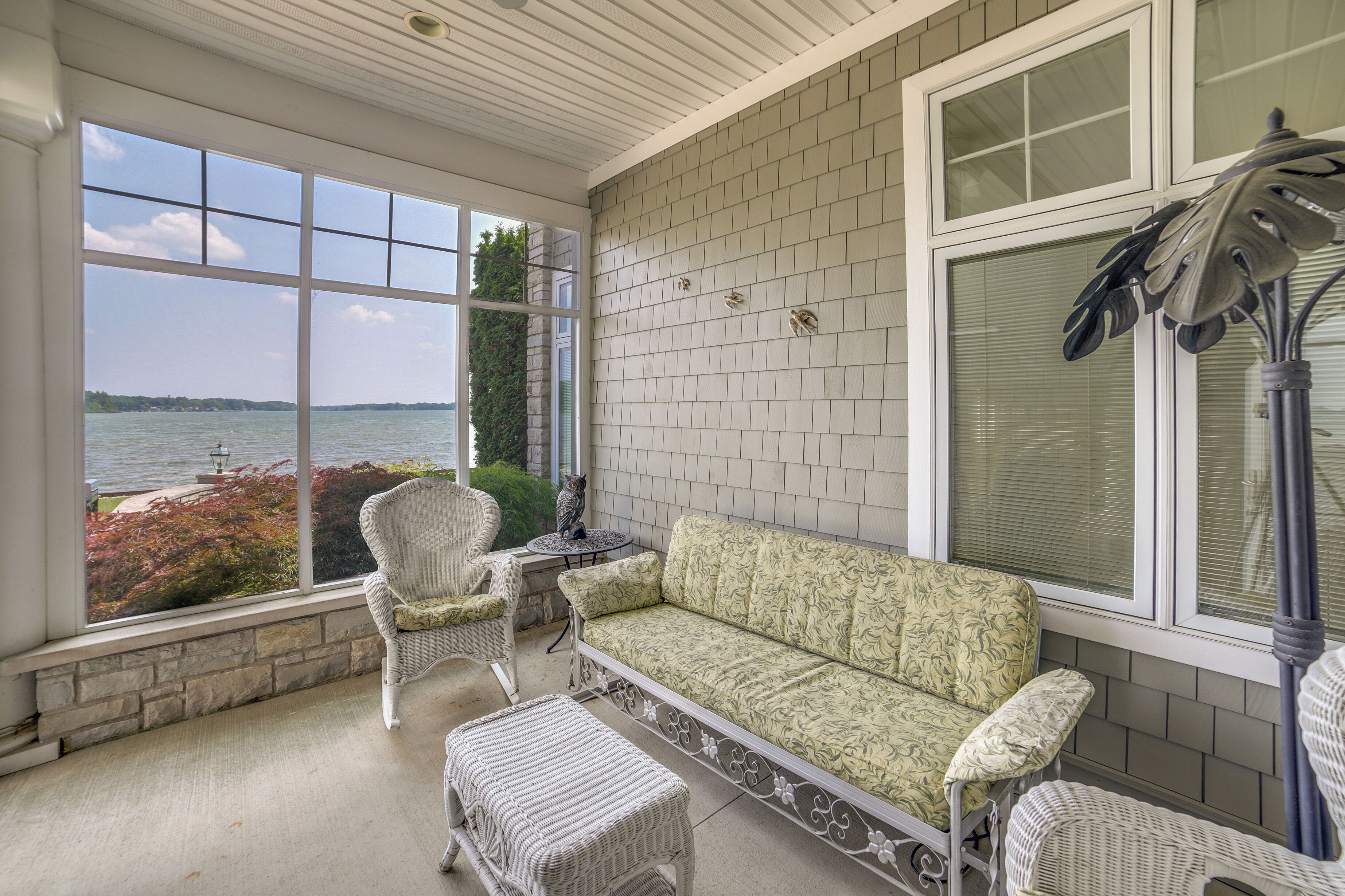 A covered patio with a view of a body of water, a white wicker sofa, and a table with chairs.