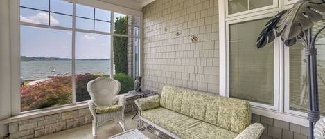 A covered patio with a view of a body of water, a white wicker sofa, and a table with chairs.