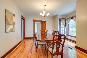 A dining room with a wooden table, chairs, a chandelier, and a vase with flowers. - New York Vacation Rental w/ Covered Porch (Geneva)