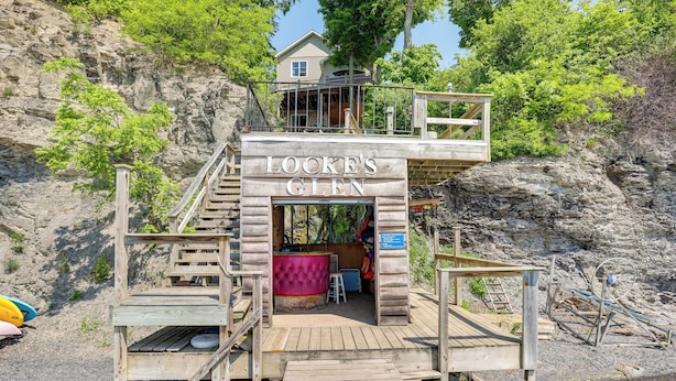 A wooden dock leading to a cabin named "Locke's Glen" with a bar area and a view of the rocky shoreline. - 'lockes Glen' - Lakefront Geneva Getaway w/ Dock! (Geneva)