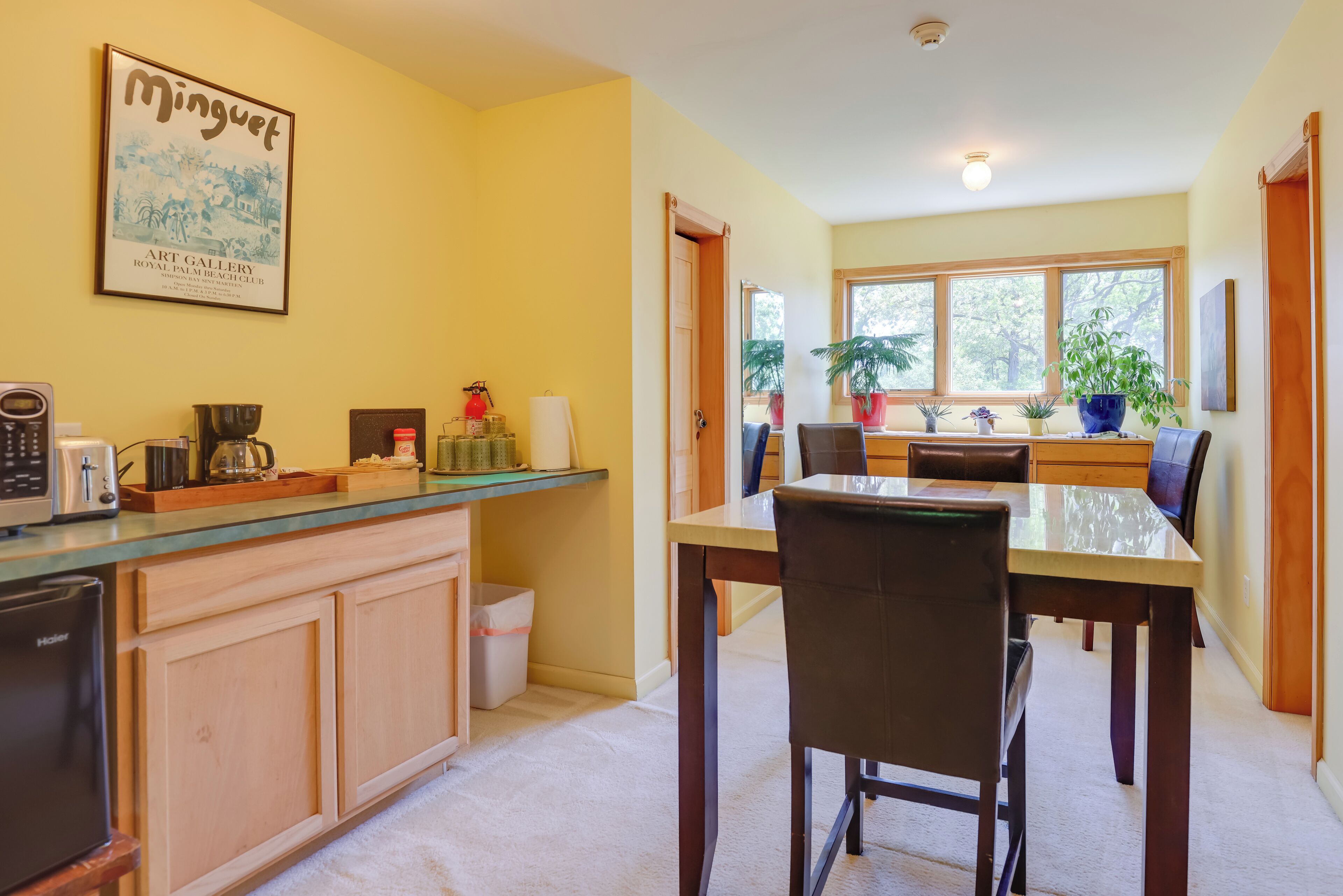 A kitchen with a dining table and chairs, a microwave, a coffee maker, and a potted plant.