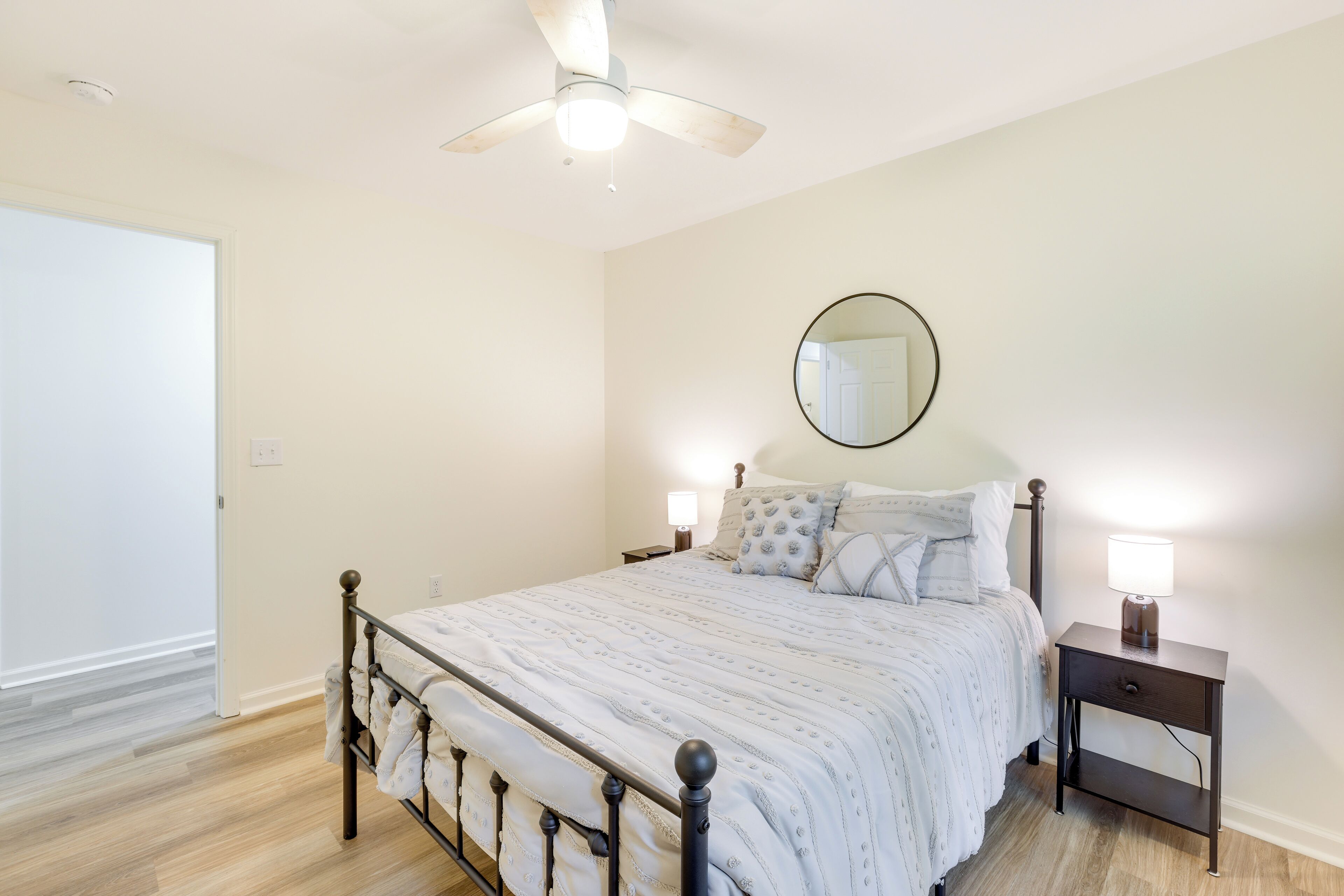 A bedroom with a bed, nightstands, a ceiling fan, a mirror, and a door.
