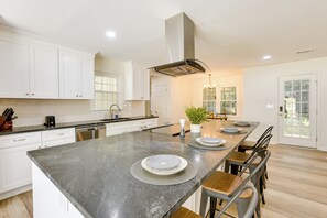 A modern kitchen with white cabinets, a granite countertop, and a central island with plates. - Northport Game Day Getaway: 5 Mi to University! (Northport)