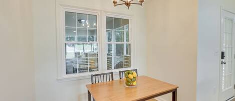 Un comedor con una mesa y sillas de madera, una araña y una ventana que ofrece vistas a muebles de exterior.