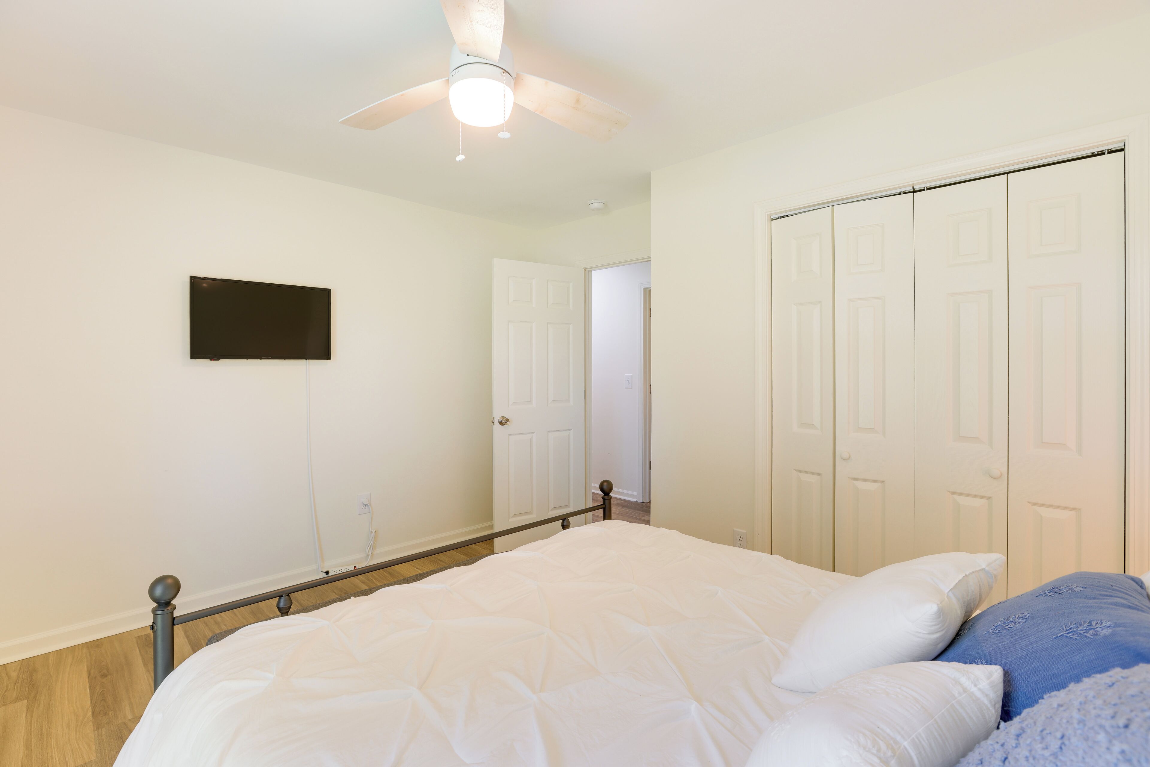 A bedroom with a bed, a ceiling fan, a TV mounted on the wall, and a closet with sliding doors.