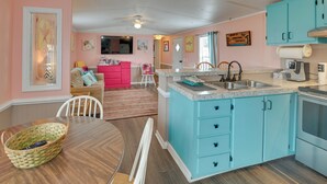 A kitchen with turquoise cabinets, a dining area with a wooden table, and a living room with a pink sofa. - Walk to Shore: Myrtle Beach House w/ Private Deck! (Murrells Inlet)