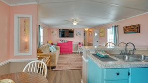 A cozy living room with a pink wall, a wooden dining table, and a red sofa. - Walk to Shore: Myrtle Beach House w/ Private Deck! (Murrells Inlet)