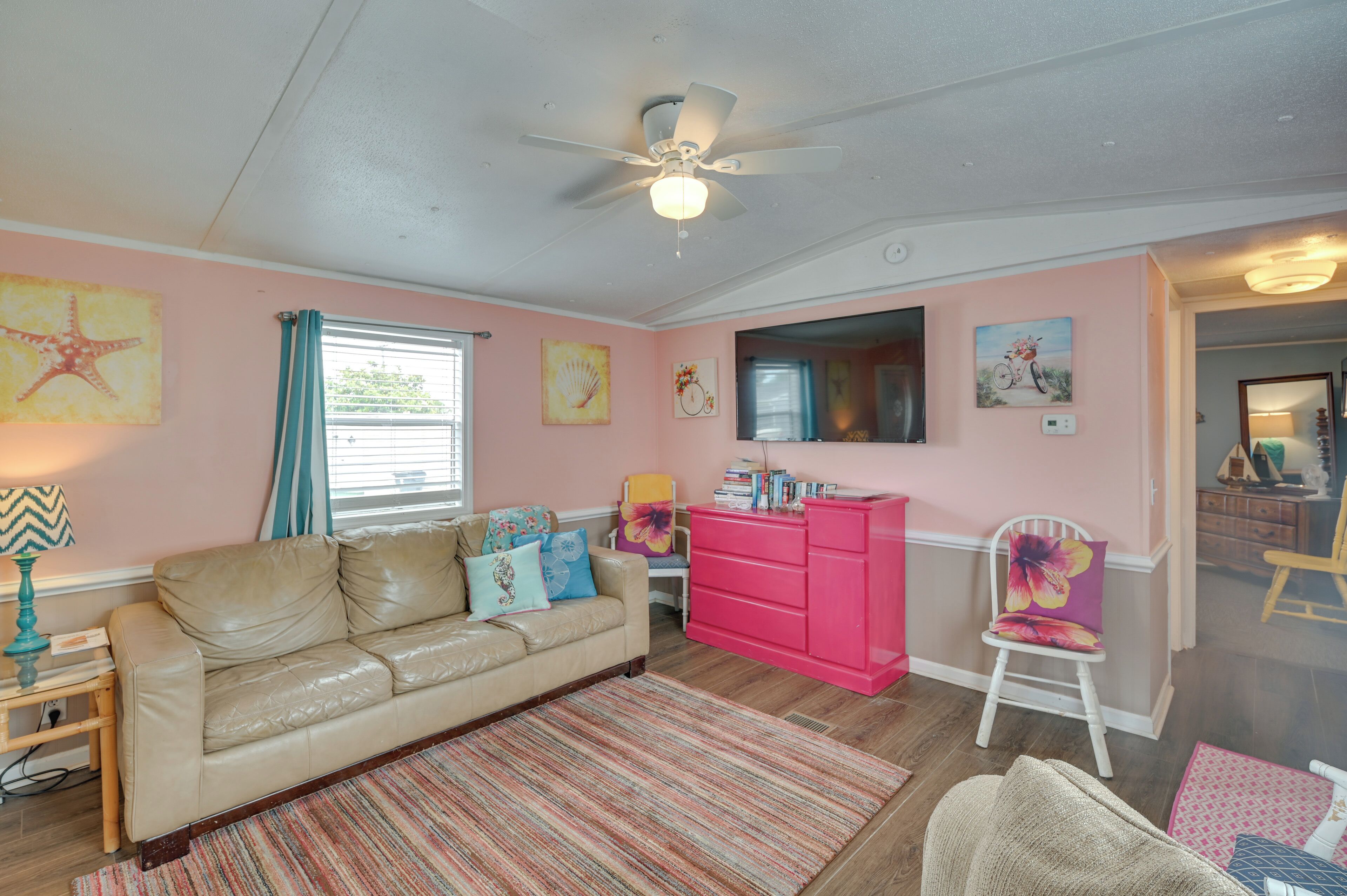 Una sala de estar con un sofá de cuero color beige, un tocador rosa y un ventilador de techo.