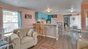 A cozy living room with a beige sofa, wooden chairs, and a kitchen area with teal cabinets and a white refrigerator. - Walk to Shore: Myrtle Beach House w/ Private Deck! (Murrells Inlet)