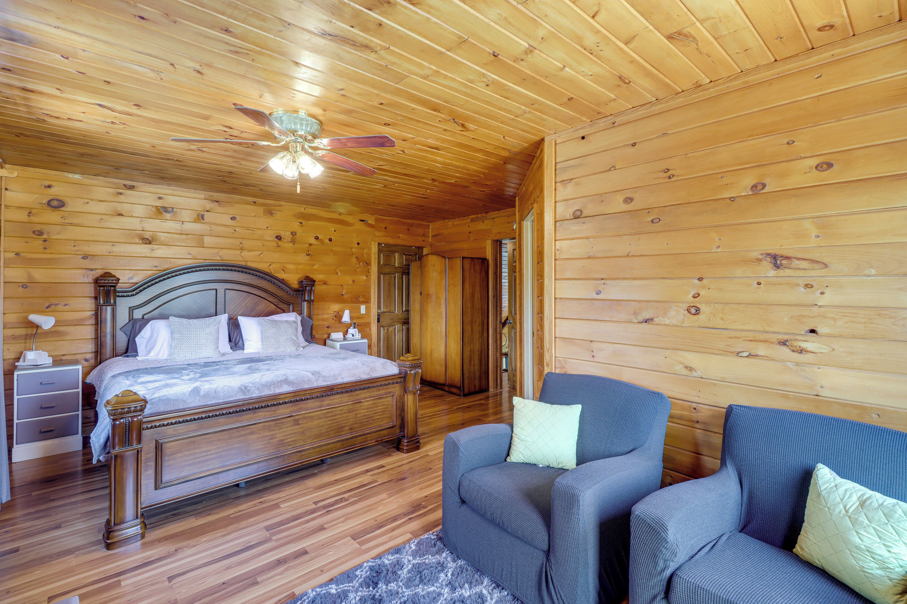 Ein Schlafzimmer mit Holzwänden, einem Bett, zwei Sesseln, einem Nachttisch und einem Deckenventilator.