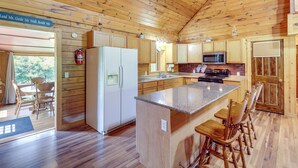 A wooden cabin interior with a kitchen featuring a refrigerator, microwave, and a large island with bar stools. - Secluded Harrison Retreat Near Buffalo Natl River (Harrison)