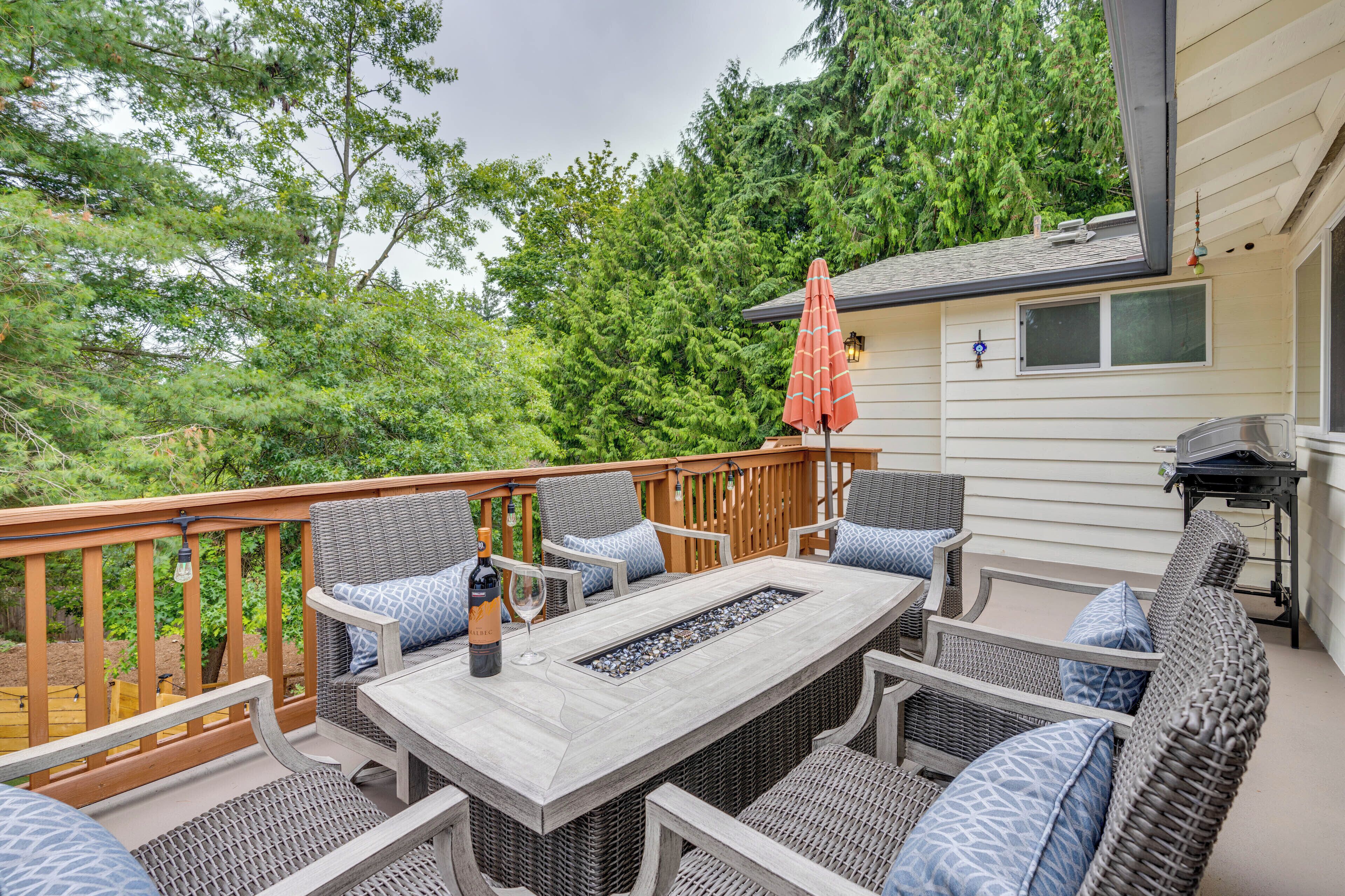 An outdoor patio with wicker furniture, a fire feature, and a red umbrella.