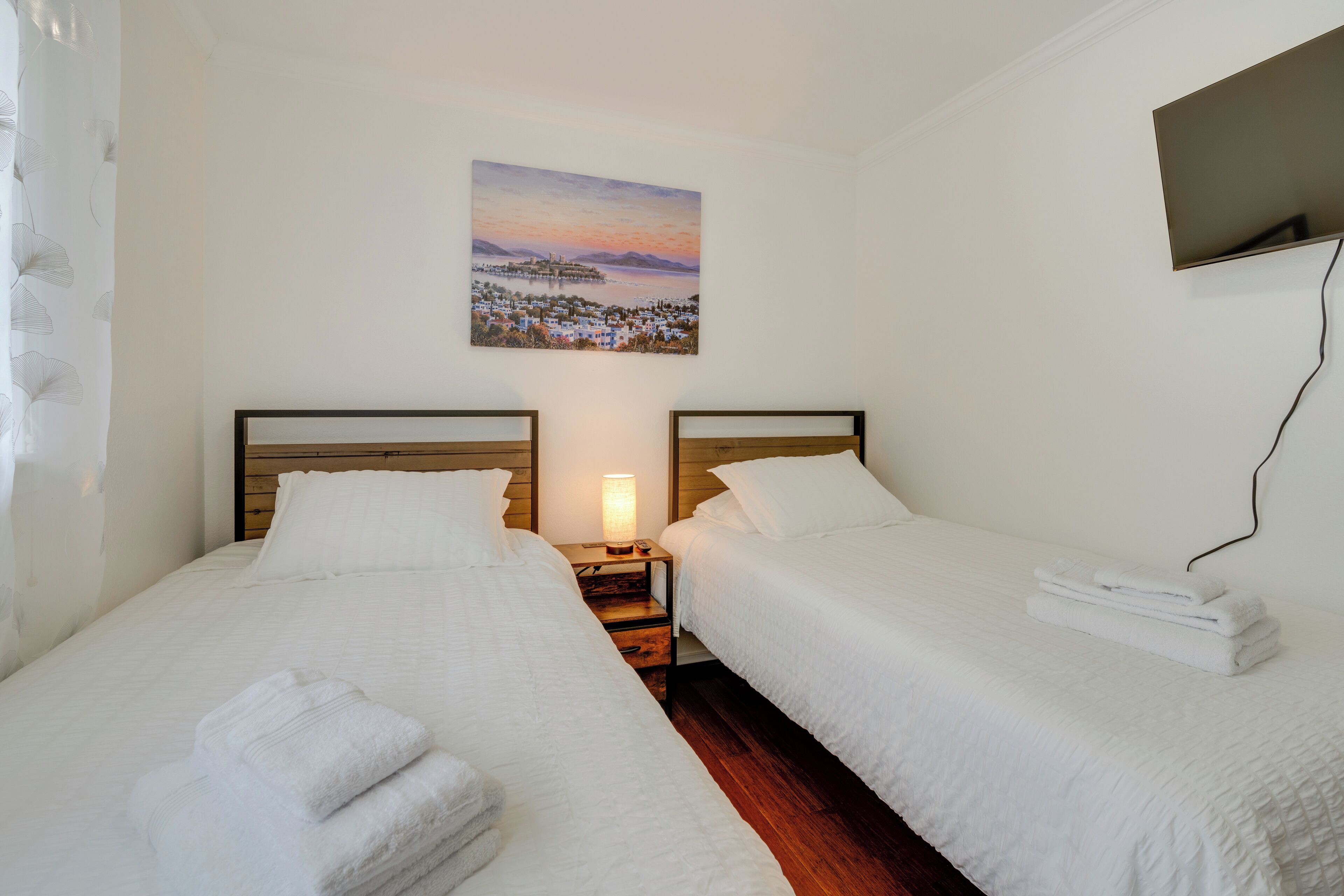 A hotel room with two beds, a nightstand with a lamp, and a painting of a landscape on the wall.