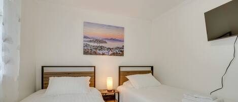 A hotel room with two beds, a nightstand with a lamp, and a painting of a landscape on the wall.