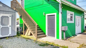 A green house with a wooden staircase leading to a gray door, a small porch, and a gravel driveway. - Walkable Paradise: Downtown Puyallup Studio! (Puyallup)