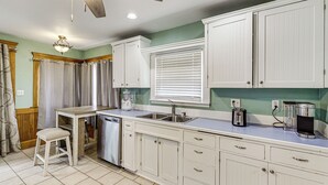 A kitchen with white cabinetry, a dishwasher, a coffee maker, and a window with blinds.