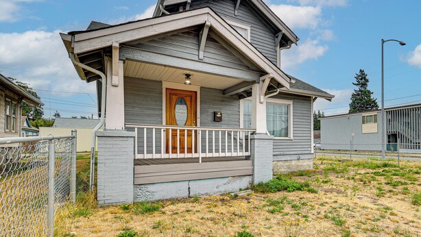 A residential house with a front porch, a wooden door, and a small fenced yard.