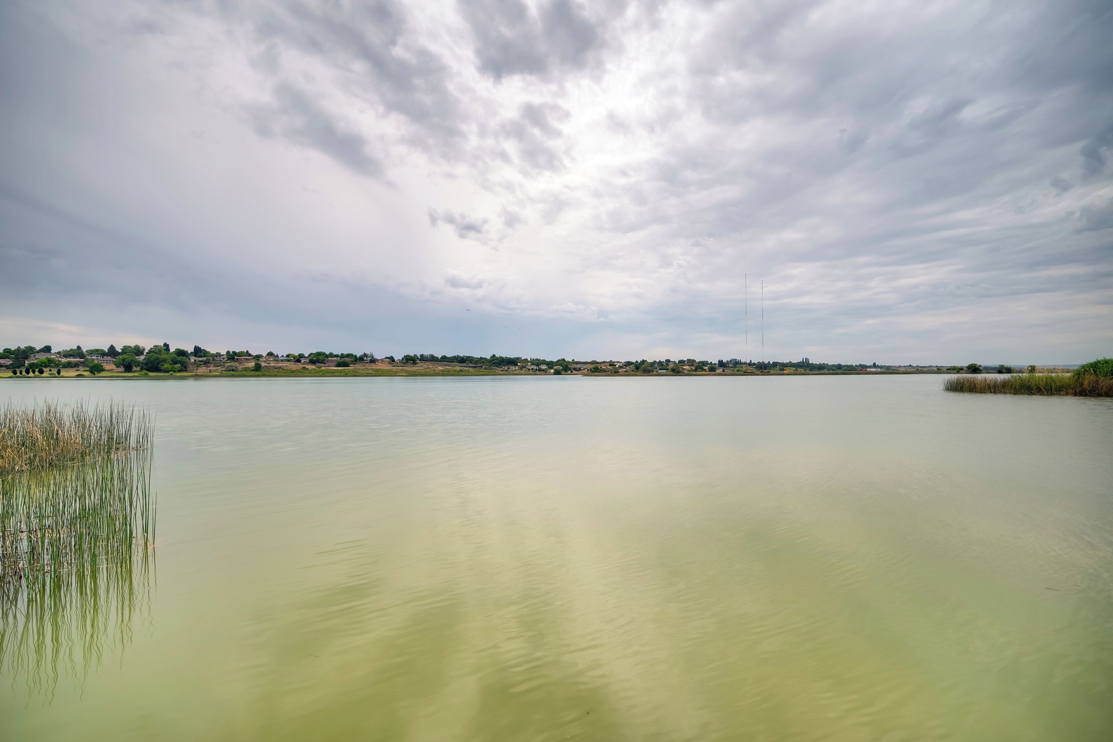 Um lago calmo com uma linha de costa distante e céu nublado.
