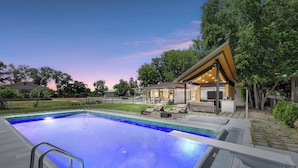 A swimming pool with a metal ladder, surrounded by a patio area with lounge chairs and a covered seating area.