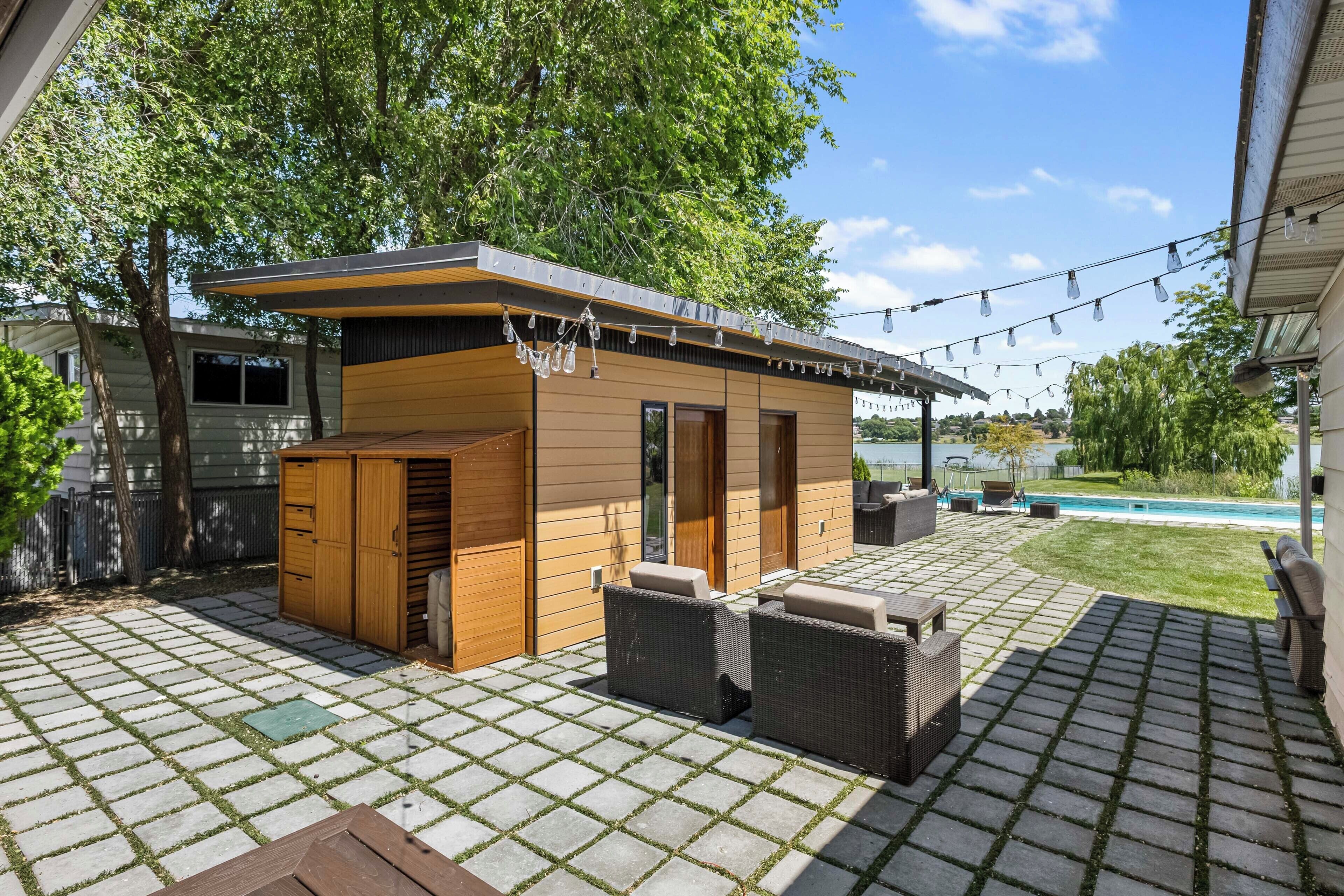 A modern outdoor patio with a wooden structure, outdoor seating, and a pool in the background.