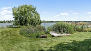 A grassy area with a pond, a willow tree, and a wooden deck.