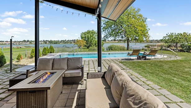An outdoor patio with a fire feature, seating, and a view of a swimming pool and landscape.