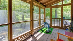 A wooden deck with large windows overlooking a forest. - Cabin w/ Hot Tub + Fishing Pond in Del Rio! (Hartford)