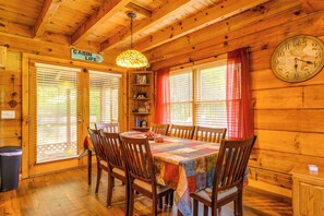 A wooden cabin interior with a dining table, chairs, a bookshelf, and a wall clock. - Cabin w/ Hot Tub + Fishing Pond in Del Rio! (Hartford)