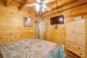 A wooden cabin room with a bed, a ceiling fan, a TV mounted on the wall, and a wardrobe. - Cabin w/ Hot Tub + Fishing Pond in Del Rio! (Hartford)