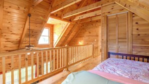 A wooden cabin room with a sloped ceiling, a bed, a window, and a door. - Cabin w/ Hot Tub + Fishing Pond in Del Rio! (Hartford)