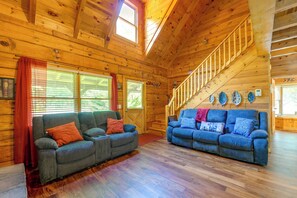 A wooden cabin interior with two sofas, a staircase, and a view of the outdoors. - Cabin w/ Hot Tub + Fishing Pond in Del Rio! (Hartford)
