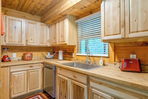 A wooden kitchen with a built-in dishwasher, a sink, and a window with blinds. - Cabin w/ Hot Tub + Fishing Pond in Del Rio! (Hartford)