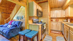 A cozy cabin interior with a sofa, bench, kitchen area, and wooden walls. - Cabin w/ Hot Tub + Fishing Pond in Del Rio! (Hartford)