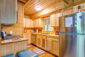 A wooden cabin interior with a kitchen area featuring a stainless steel refrigerator, wooden cabinets, and a built-in oven. - Cabin w/ Hot Tub + Fishing Pond in Del Rio! (Hartford)