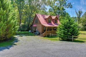 A rustic cabin with a red roof, surrounded by dense green trees and a gravel driveway. - Cabin w/ Hot Tub + Fishing Pond in Del Rio! (Hartford)