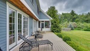 Um deck coberto com móveis de exterior, teto de madeira e vista para um jardim exuberante e árvores.