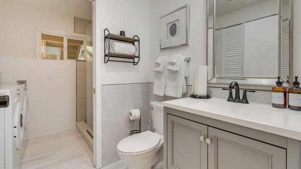 A modern bathroom with a toilet, sink, and shower. There is a towel rack, a framed picture, and a mirror. - Cozy Kenmore Vacation Rental w/ Shared Hot Tub! (Kenmore)