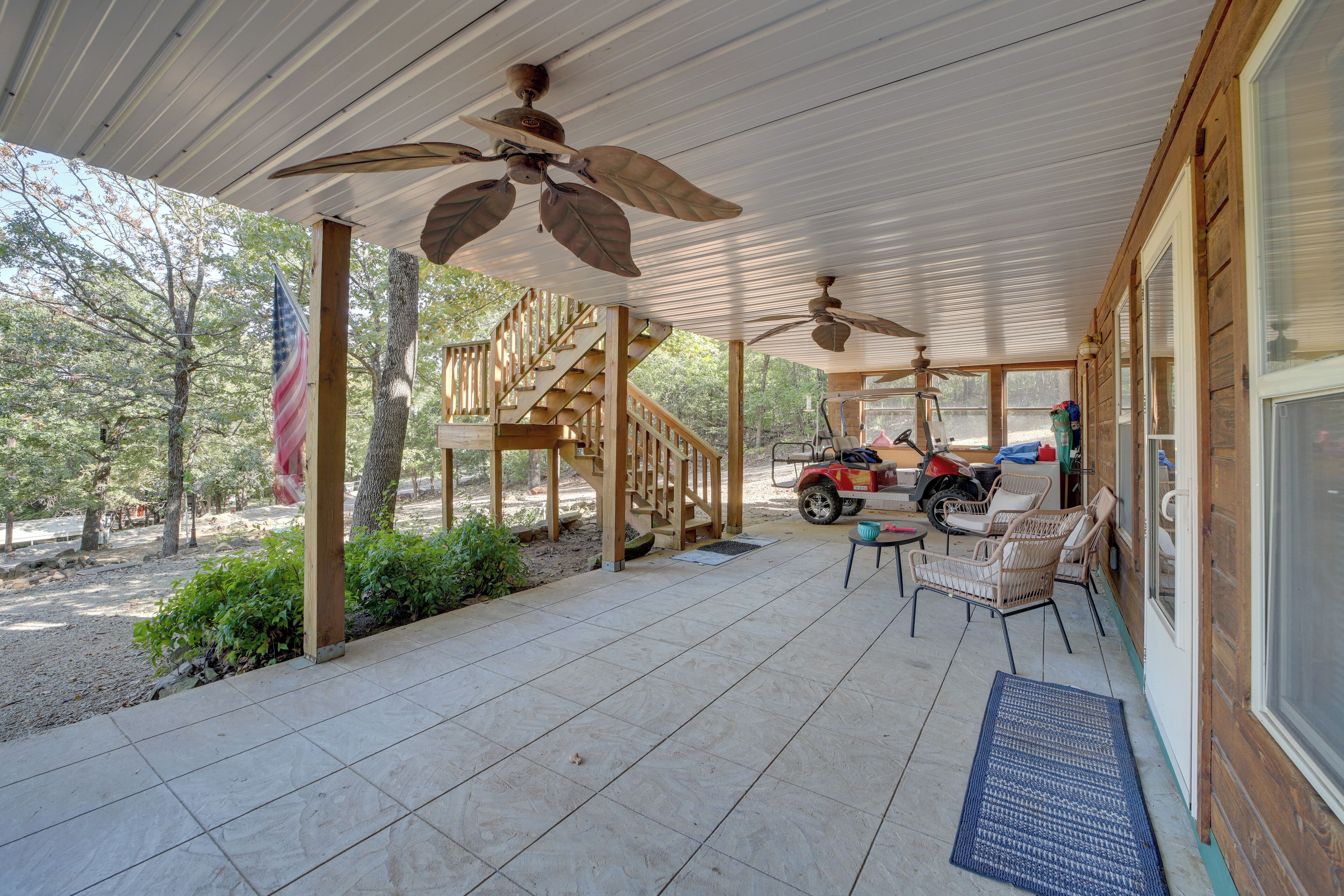 A covered patio with ceiling fans, a wooden staircase, outdoor seating, and a parked vehicle.