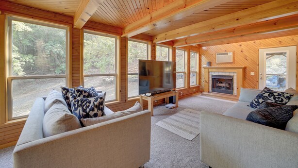 A cozy cabin interior with a fireplace, large windows, and a television. - Lake Eufaula Retreat w/ Boat Slip & Fireplace! (Stigler)