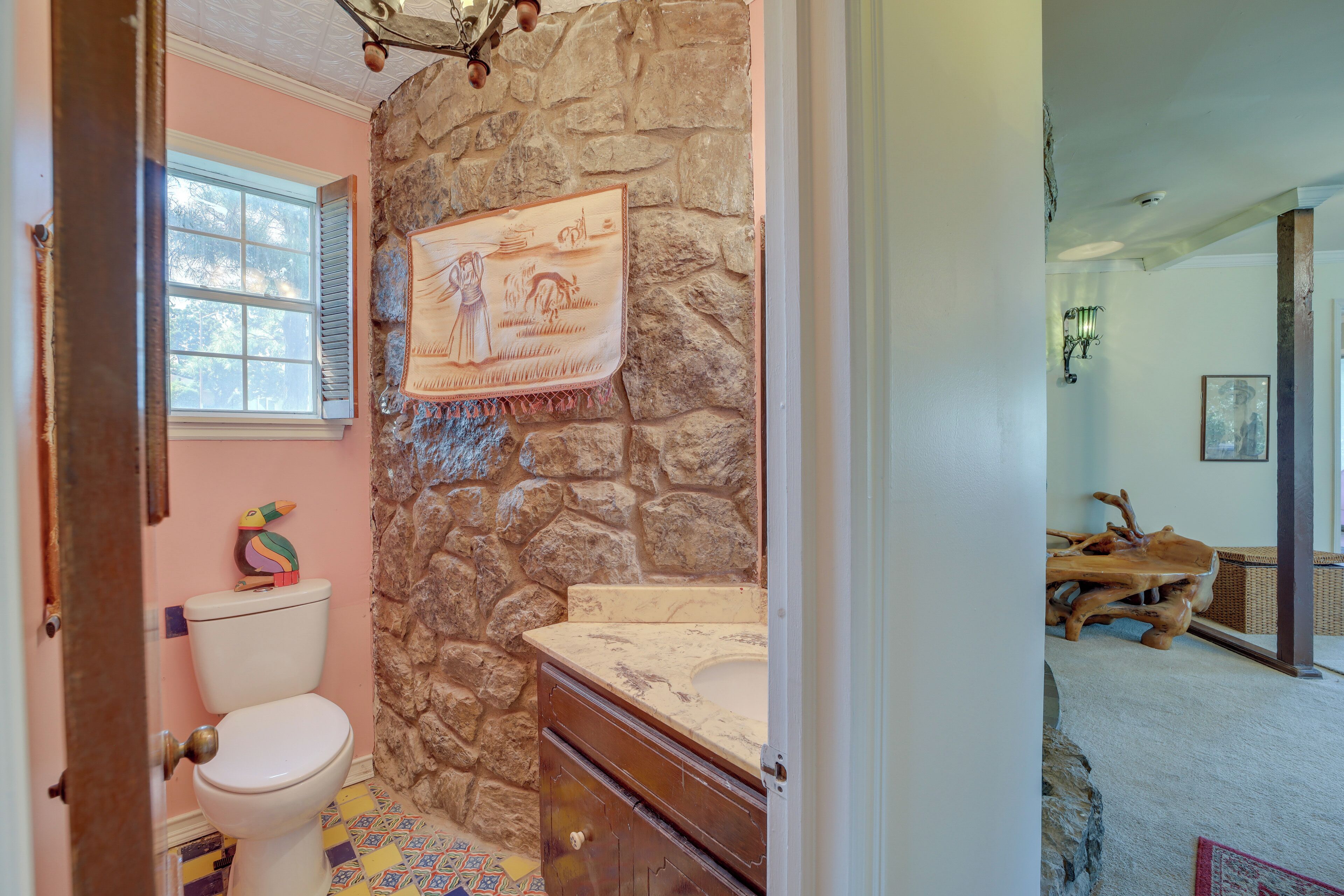 A bathroom with a stone wall, a wooden vanity, and a colorful tiled floor.